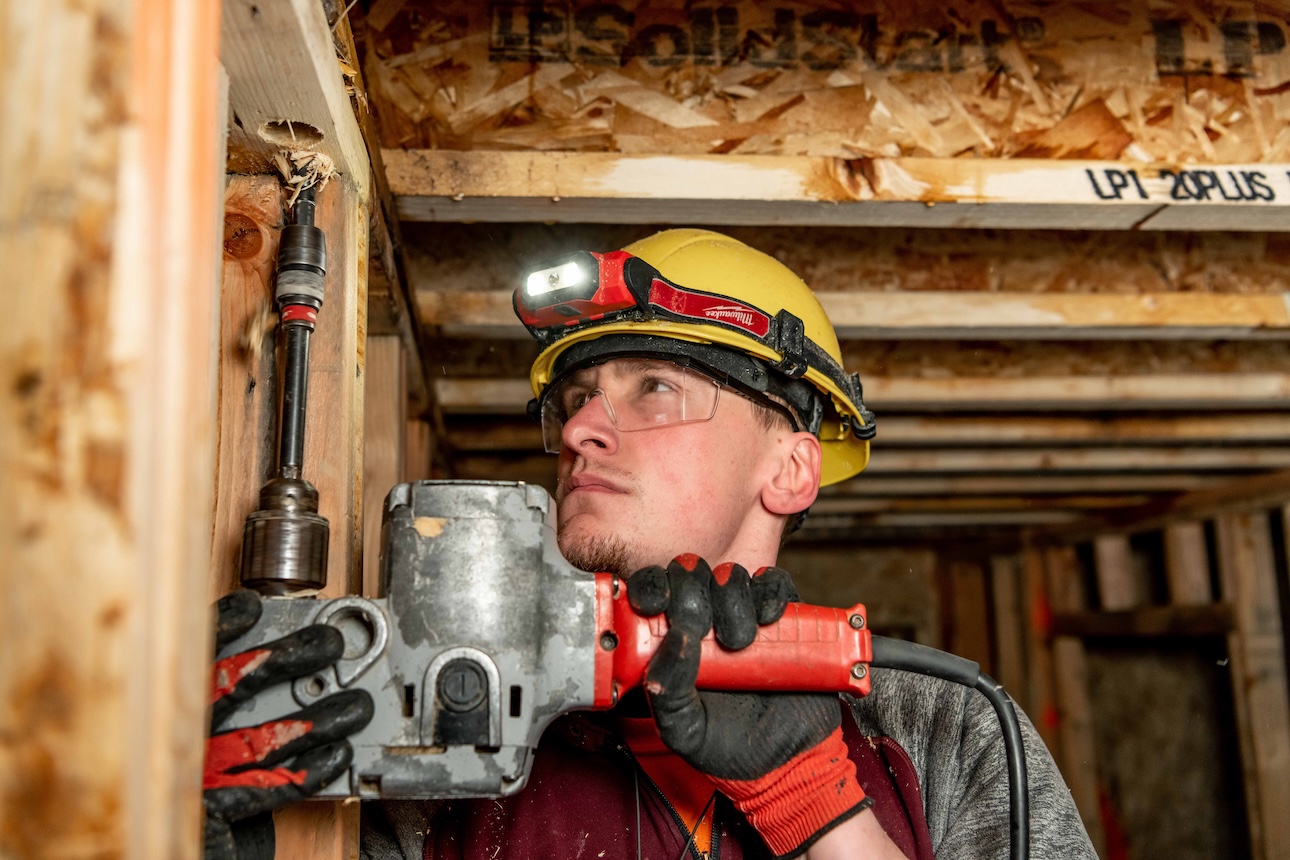 A man wearing a hard hat and safety glasses using a drill.