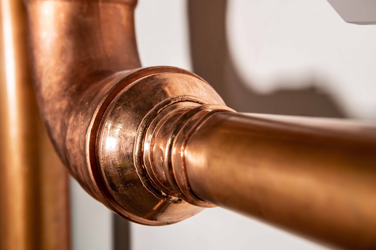 A close-up of a copper pipe and a wall.