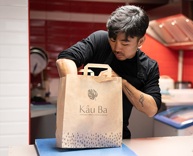 Kau Ba's new branding shown on a takeout bag being filled by a male server